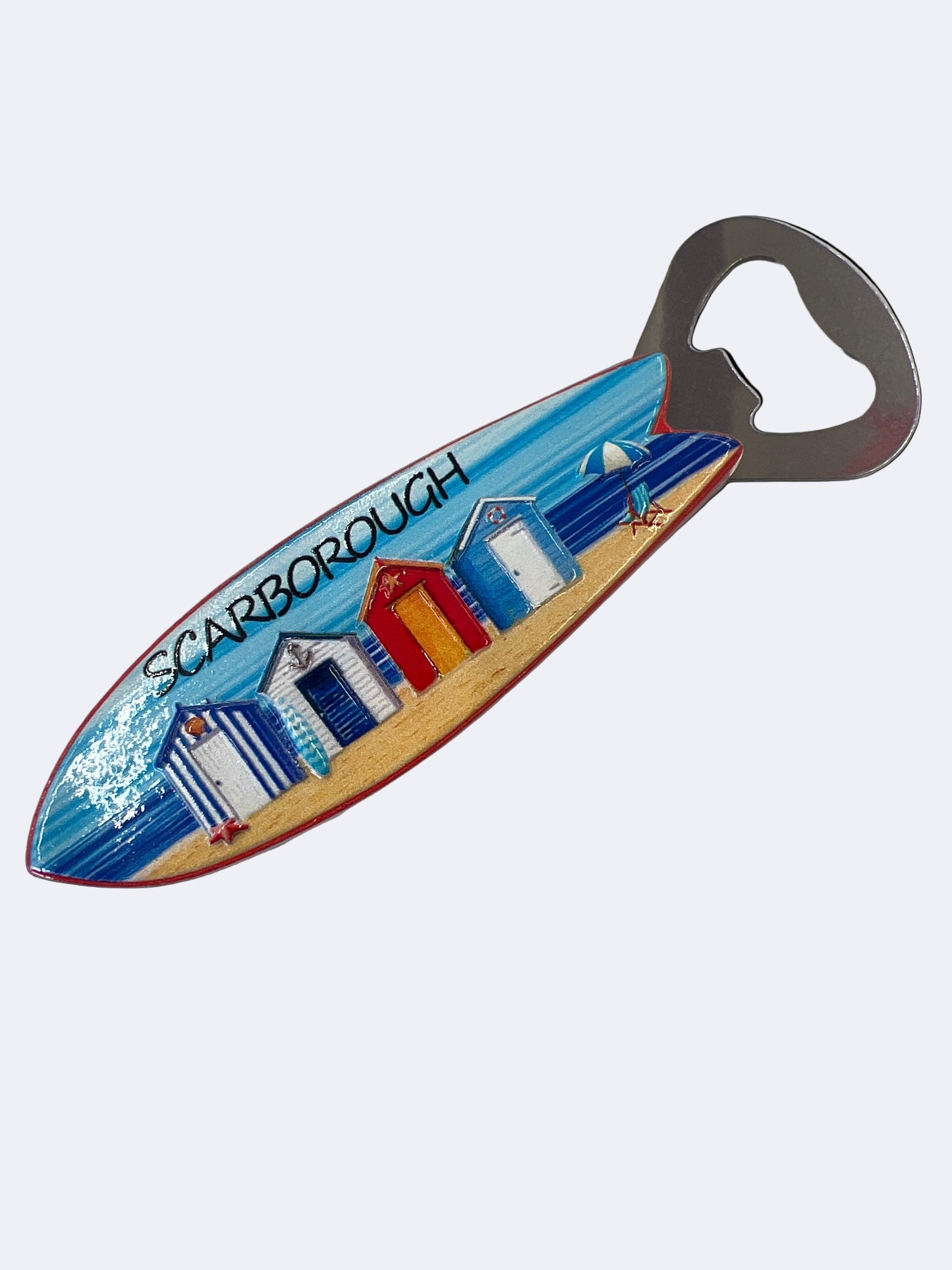 A multicolored surfboard-shaped magnet with a beach and houses design, and a built-in bottle opener.