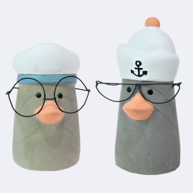 Two stone seagull figurines, one with a white cap and the other with a grey cap, both wearing glasses and seated.