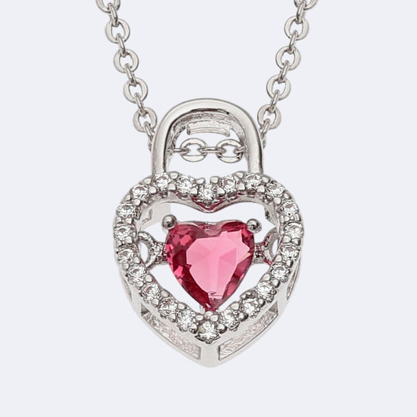 A silver-colored heart-shaped necklace with a red inset glass stone and adorned with clear stones on a trace chain.
