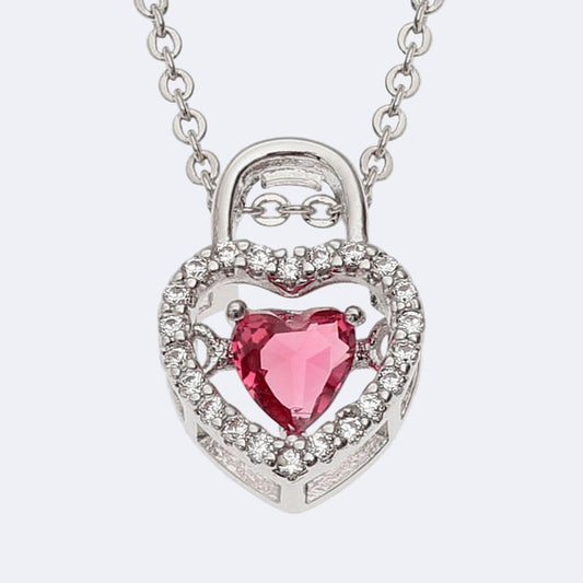 A silver-colored heart-shaped necklace with a red inset glass stone and adorned with clear stones on a trace chain.