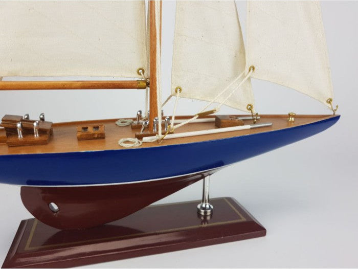 Model sailboat with blue hull and white sails on a white background