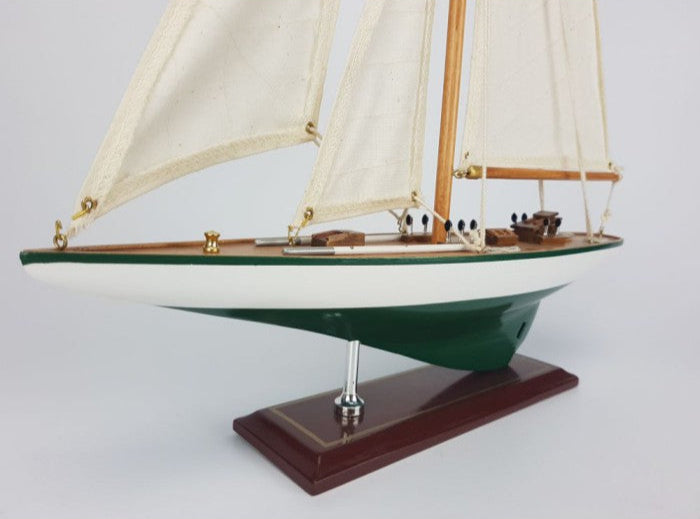 Model sailboat with green hull and white sails on a gray background