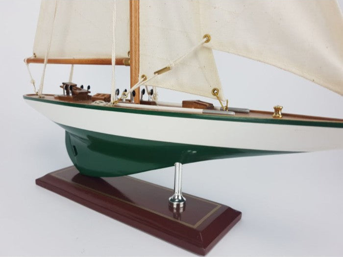 Model sailboat with green hull and white sails on a wooden base against a white background