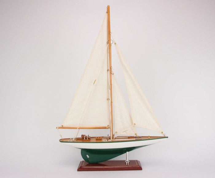 Model sailboat with green hull and white sails on a gray background