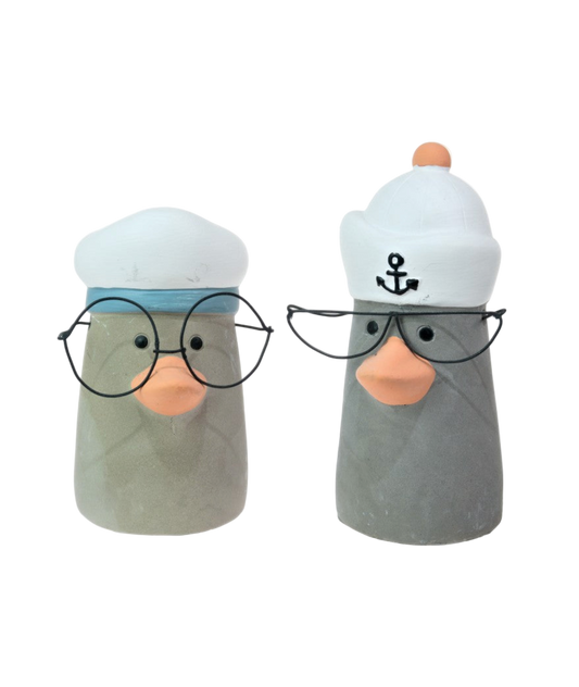 Two ceramic ducks wearing sailor hats and glasses on a white background